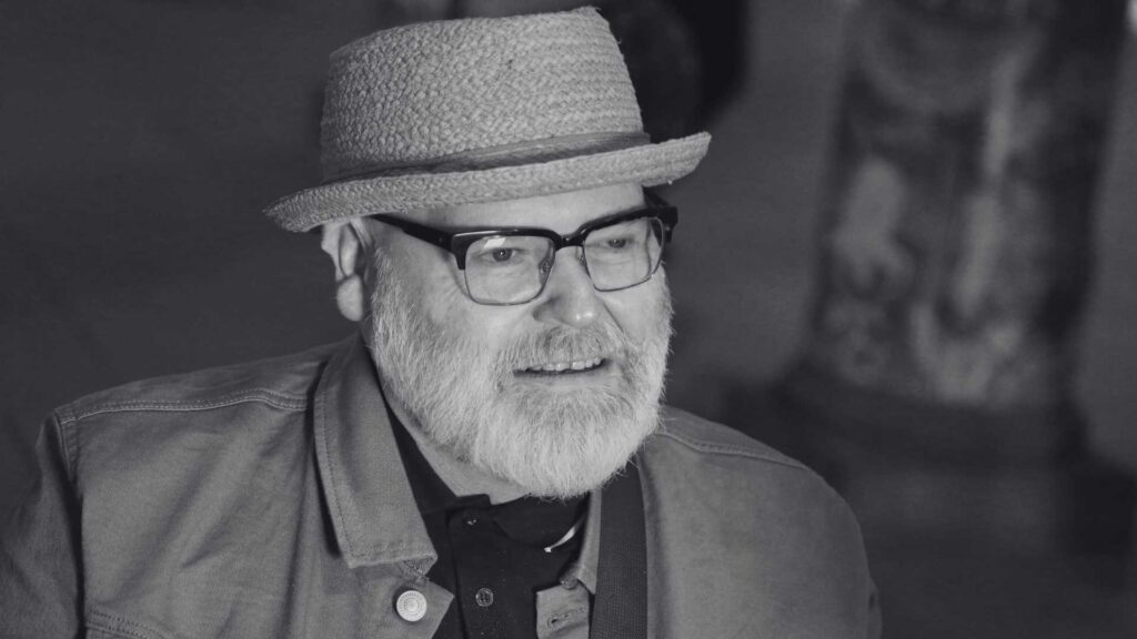 Photo showing the artist wearing a hat, black spectacles and a beard, looking at his artwork