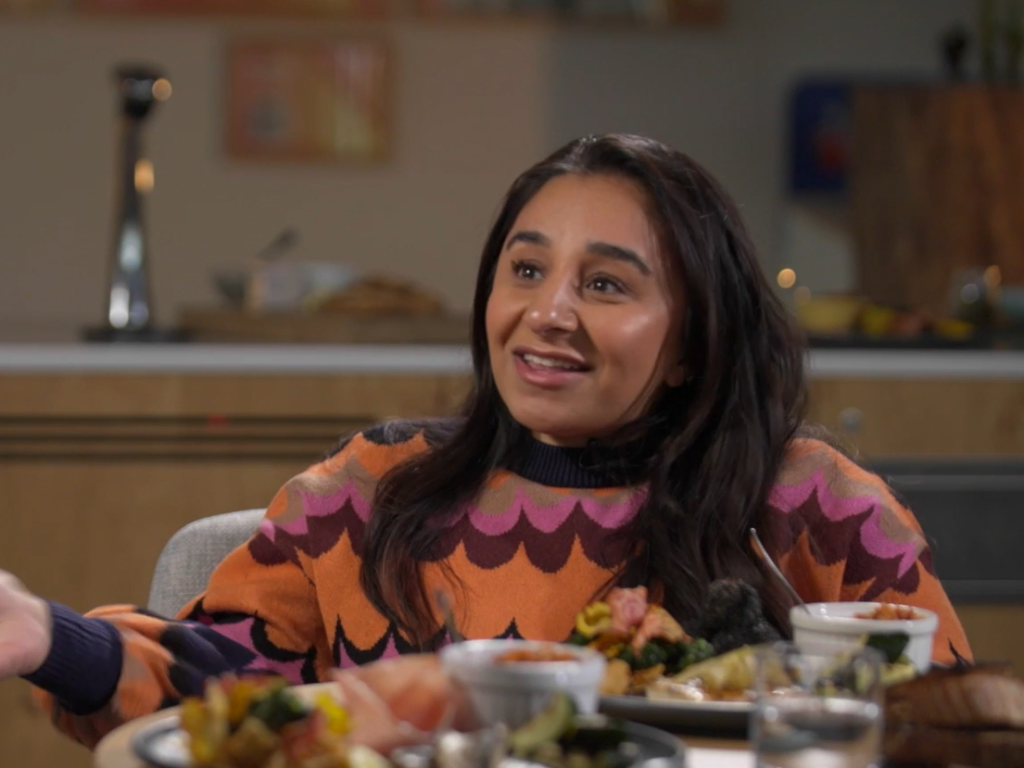 South Asian woman smiling and talking , wearing a colourful jumper
