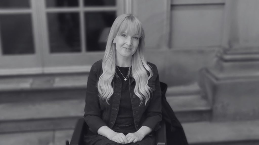 An image of a woman with long blonde hair seated in a wheelchair