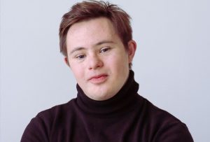 A young man with short brown hair, wearing a black roll neck jumper. He has Down Syndrome.