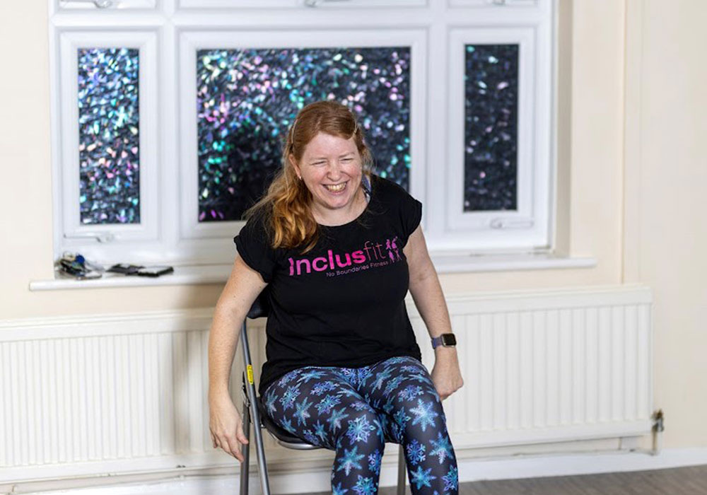 Sam sat teaching, having a laugh. Sam is wearing snowflake leggings and a black Inclusfit top.