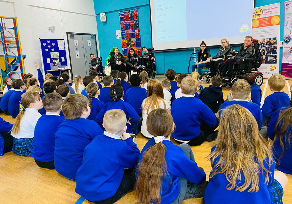 School pupils in blue uniform looking forward towards members of the Happy Smiles Training team delivering a workshop in a school hall setting