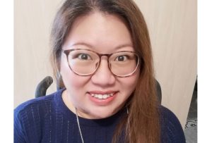 An East-Asian woman with smooth long hair cascading over her shoulder. She wears a navy blue sweater. Her smile is warm and genuine. Her almond-shaped eyes, framed by glasses, radiate curiosity and enthusiasm.