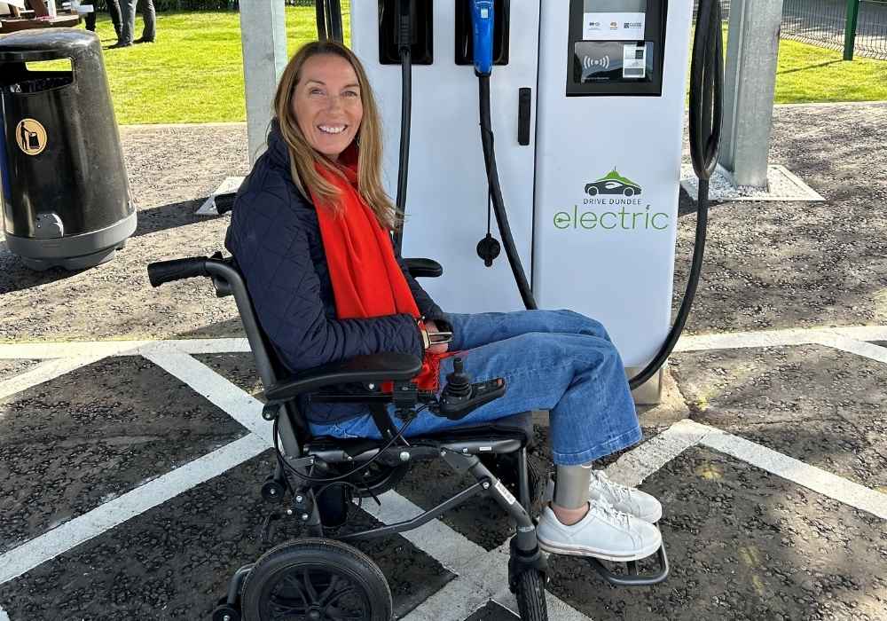 White woman with blonde hair using a wheelchair sitting in front of an EV charger