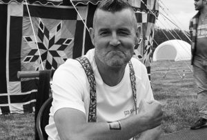 An image of Mark Webb posing with a temporary tattoo. His hair is styled in a mohican and his expression is happy yet resolute.